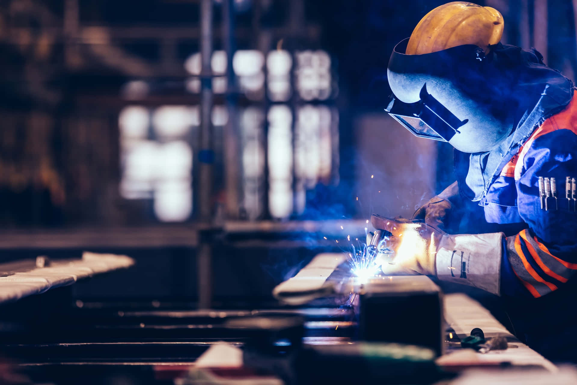 A Worker Welding Metal In A Factory Background