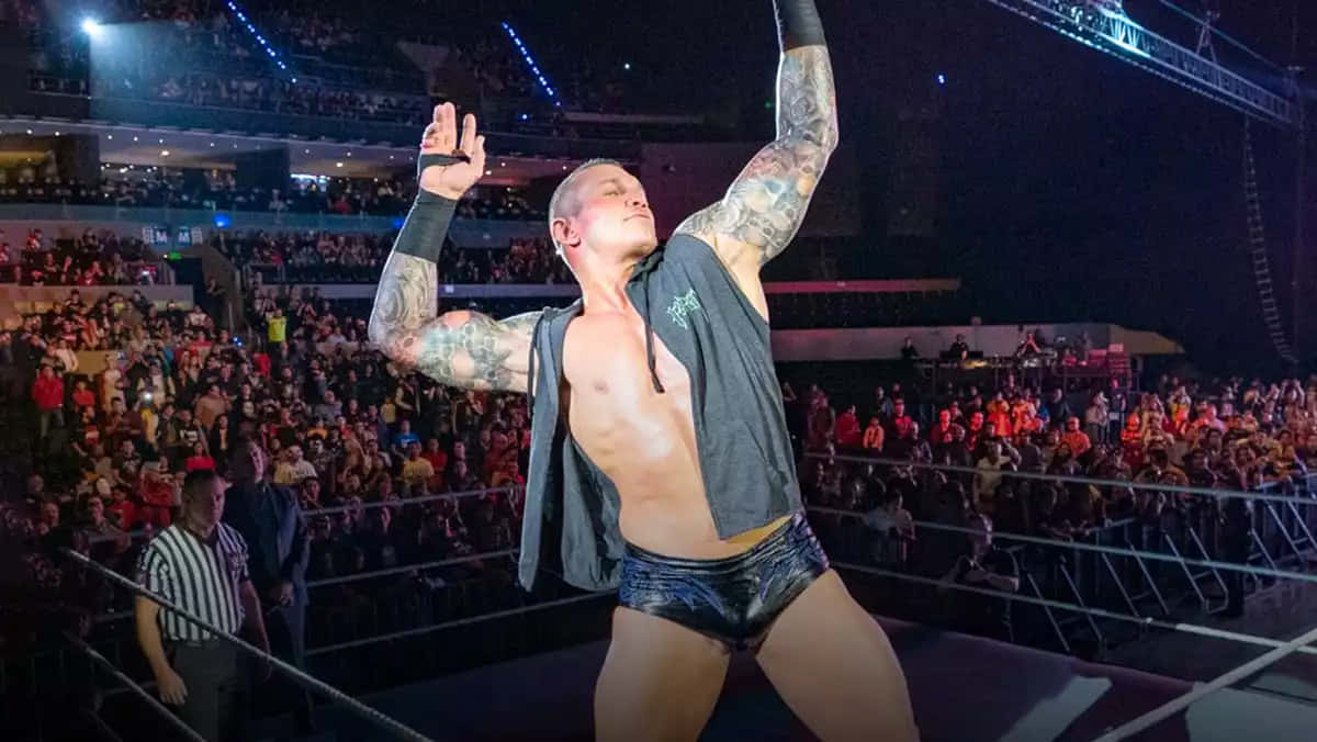 A Wrestler Is Holding His Arms Up In The Air Background