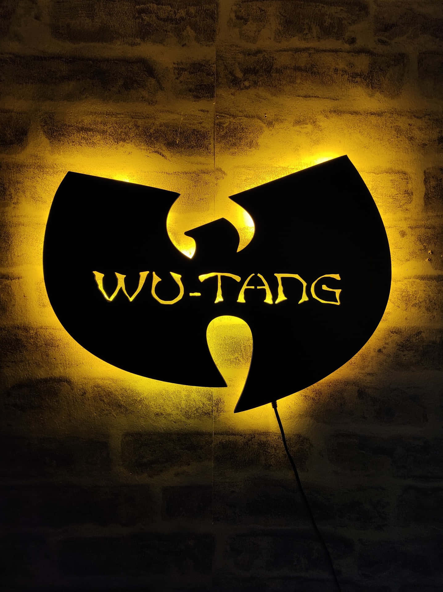 A Wutang Logo Is Illuminated On A Brick Wall Background