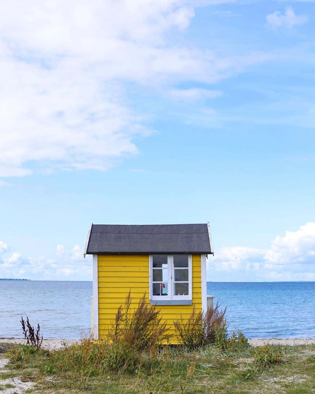 A Yellow Beach Hut Sits On The Shore Background