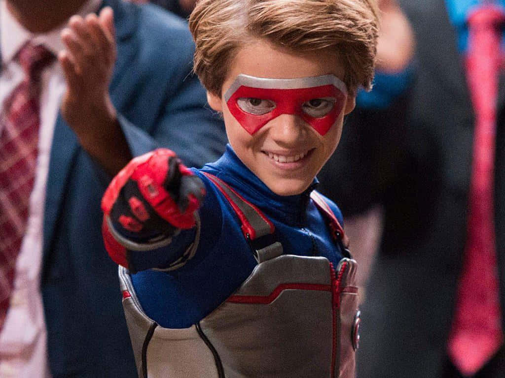 A Young Boy In A Superhero Costume Is Pointing At The Crowd Background