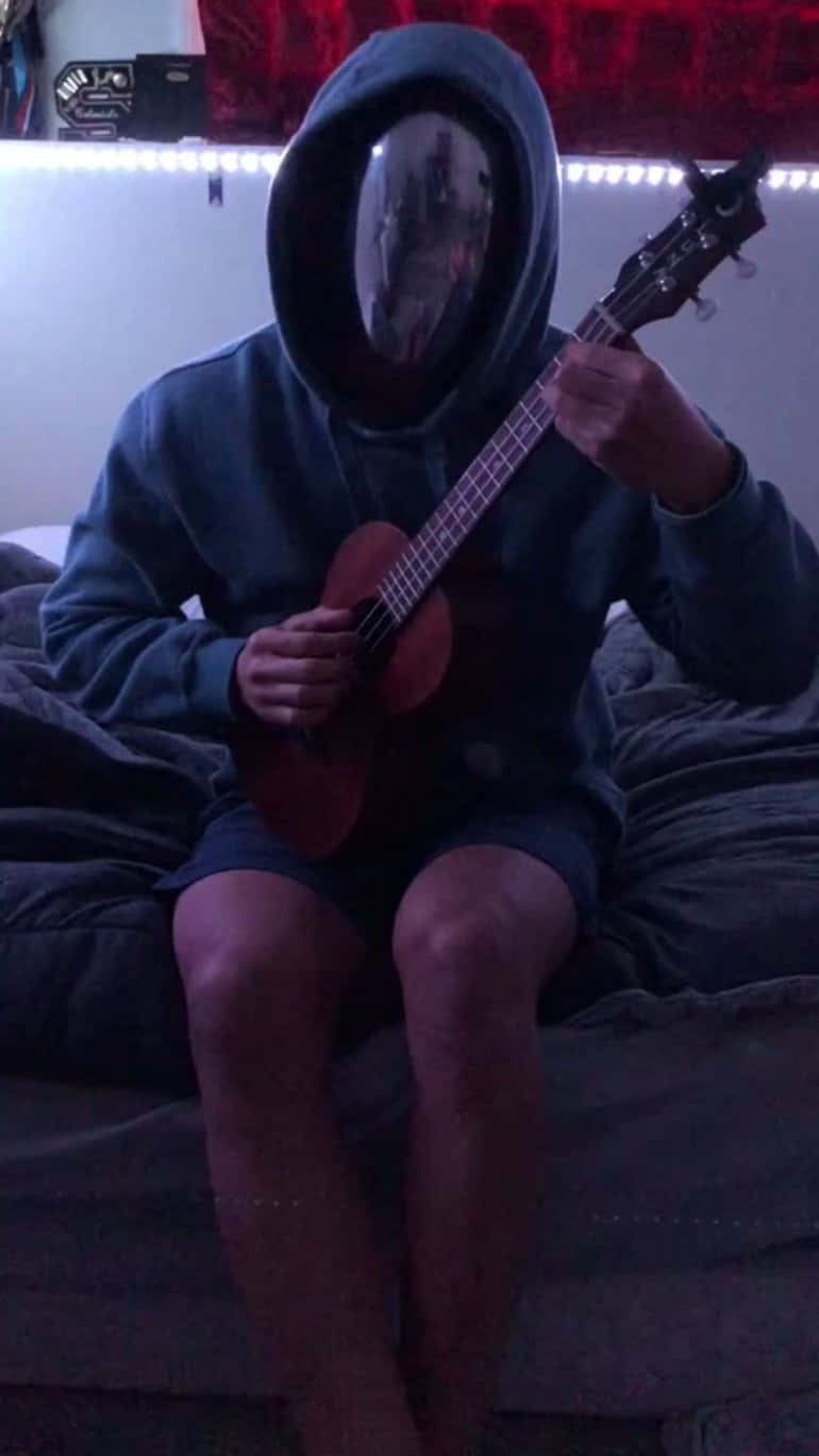 A Young Boy Strums His Ukulele, Bringing Light And Joy To His Music. Background