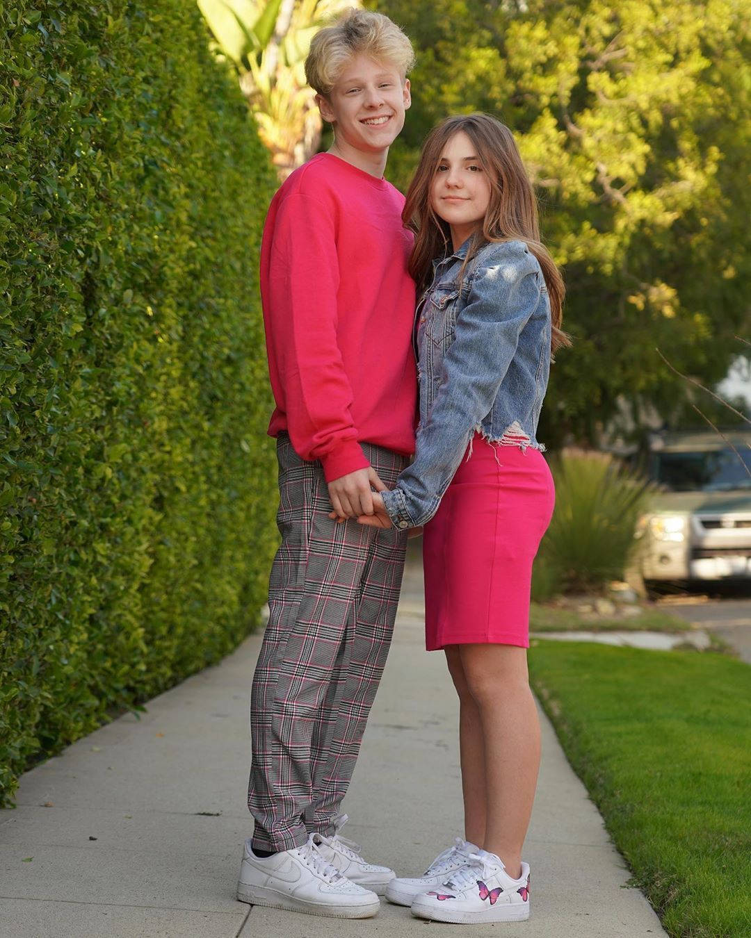 A Young Couple Standing On A Sidewalk Background