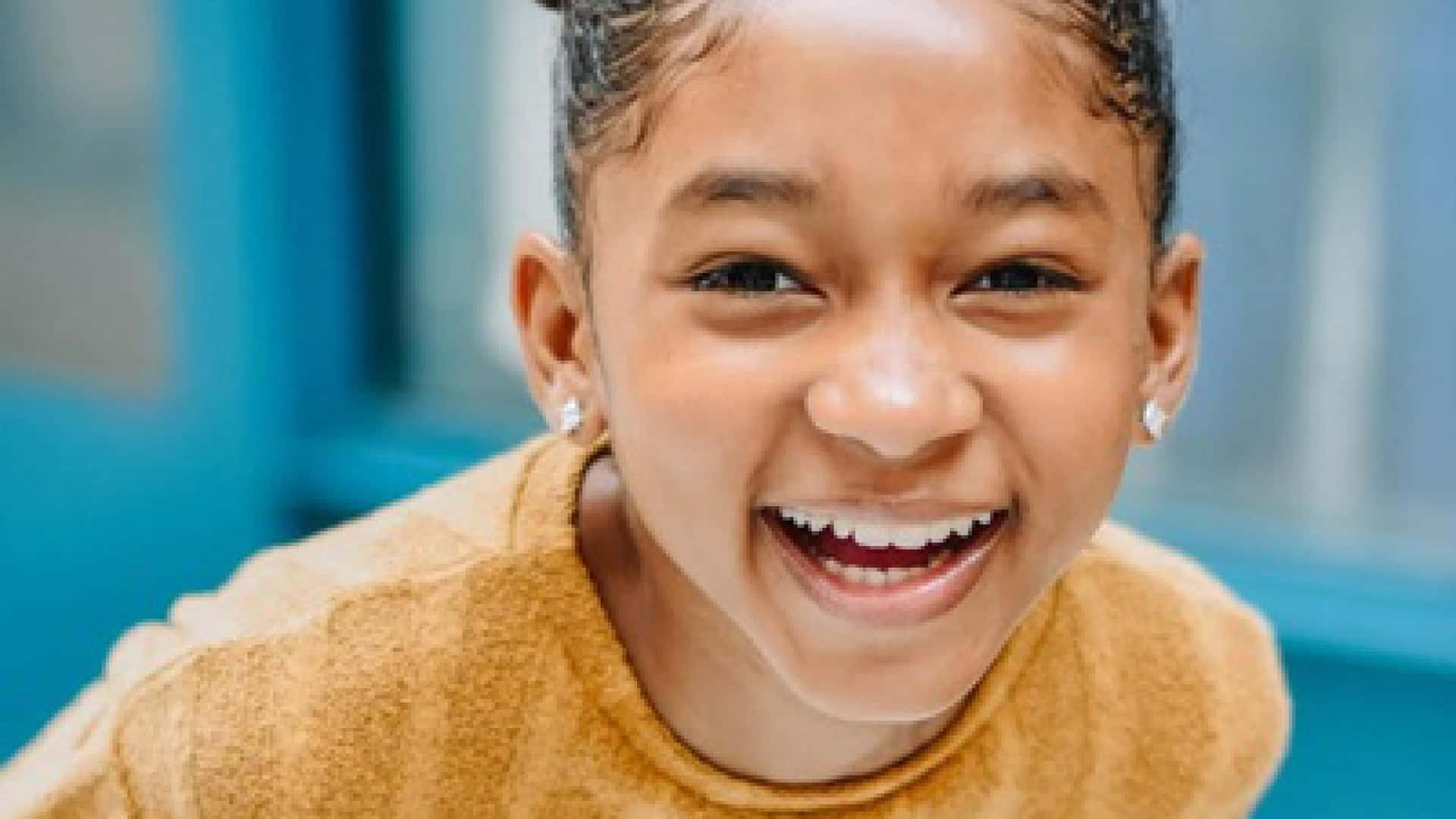 A Young Girl Is Smiling While Sitting On A Chair Background