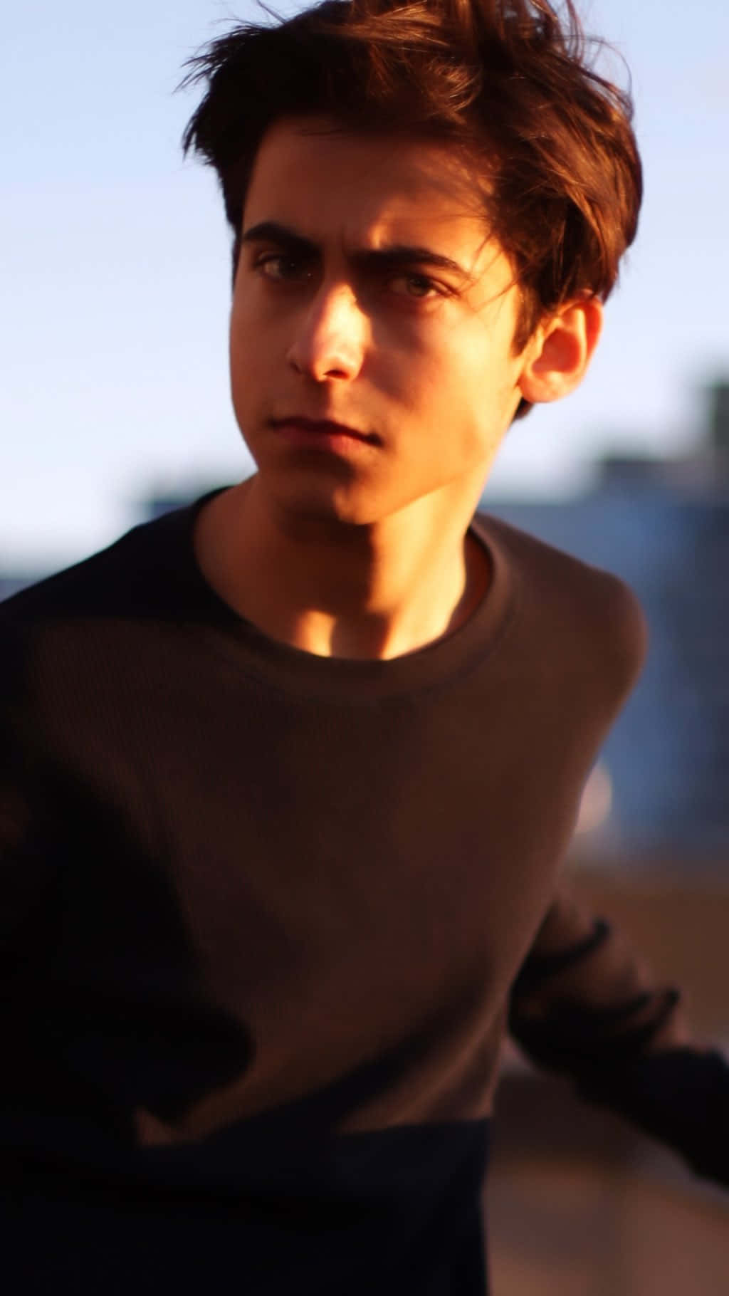 A Young Man In A Black Shirt Is Looking At The Camera Background