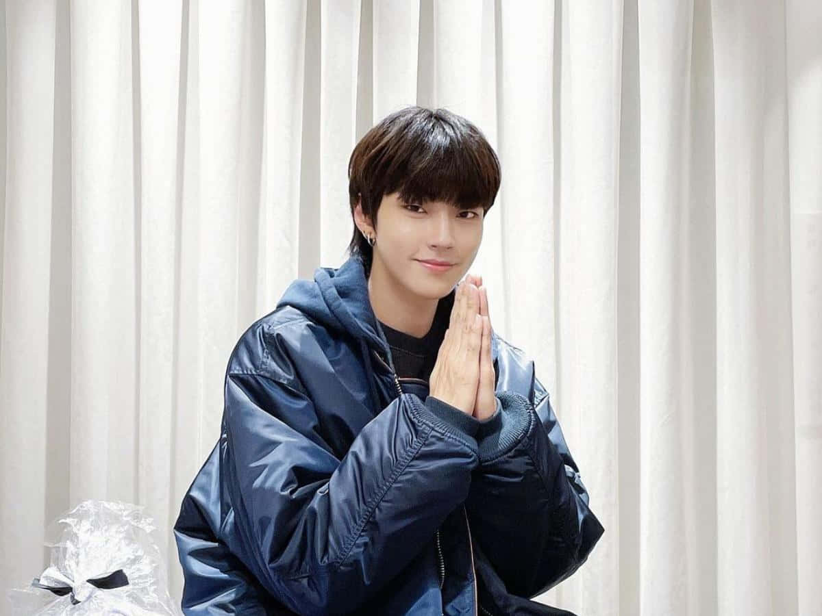 A Young Man In A Blue Jacket Is Sitting On A Chair Background