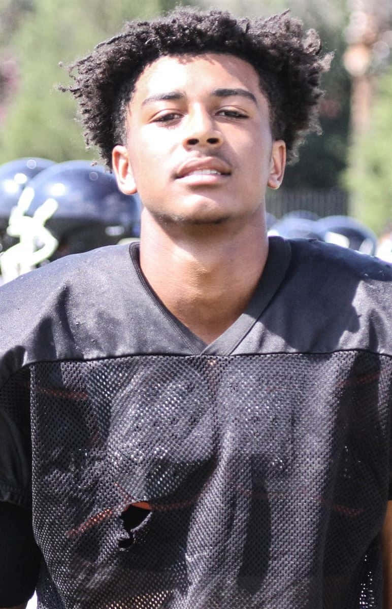 A Young Man In A Football Uniform Standing On The Field Background