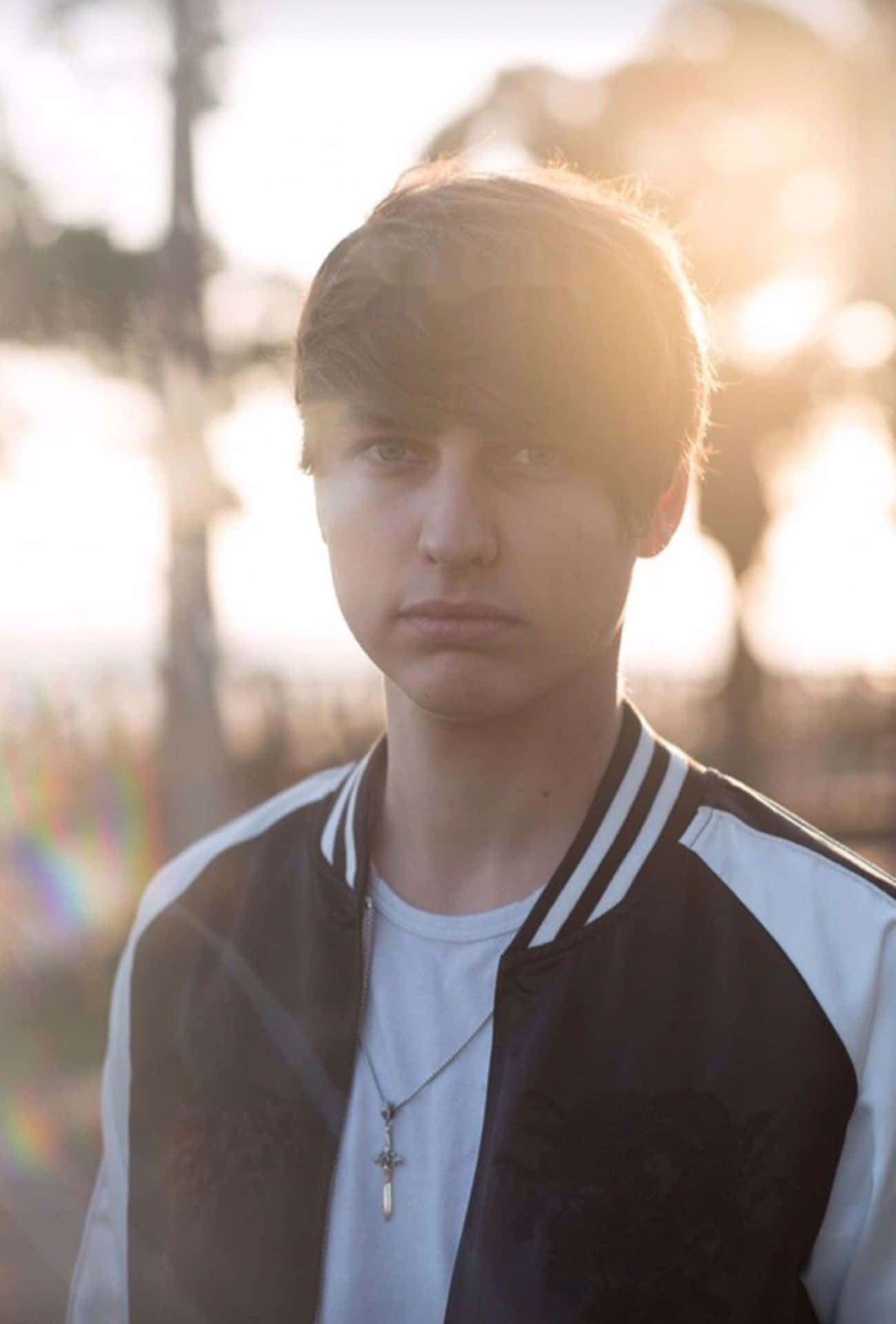 A Young Man In A Jacket Standing In The Sun Background