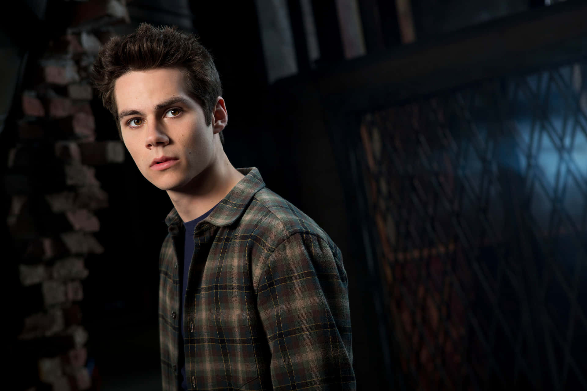 A Young Man In A Plaid Shirt Is Standing In Front Of A Brick Wall Background