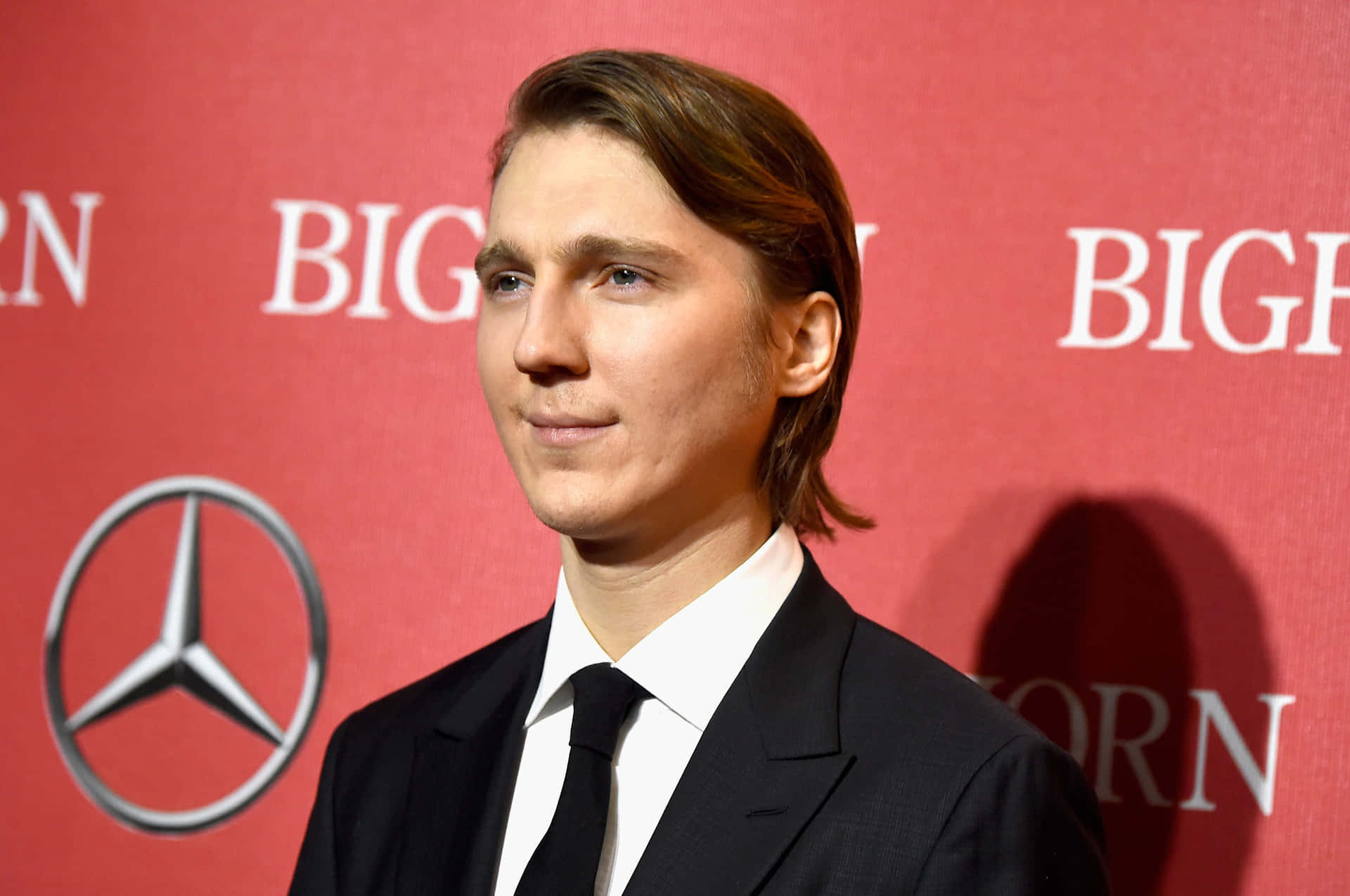 A Young Man In A Suit And Tie Standing In Front Of A Red Wall Background