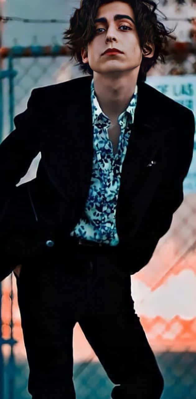 A Young Man In A Suit Leaning Against A Fence Background
