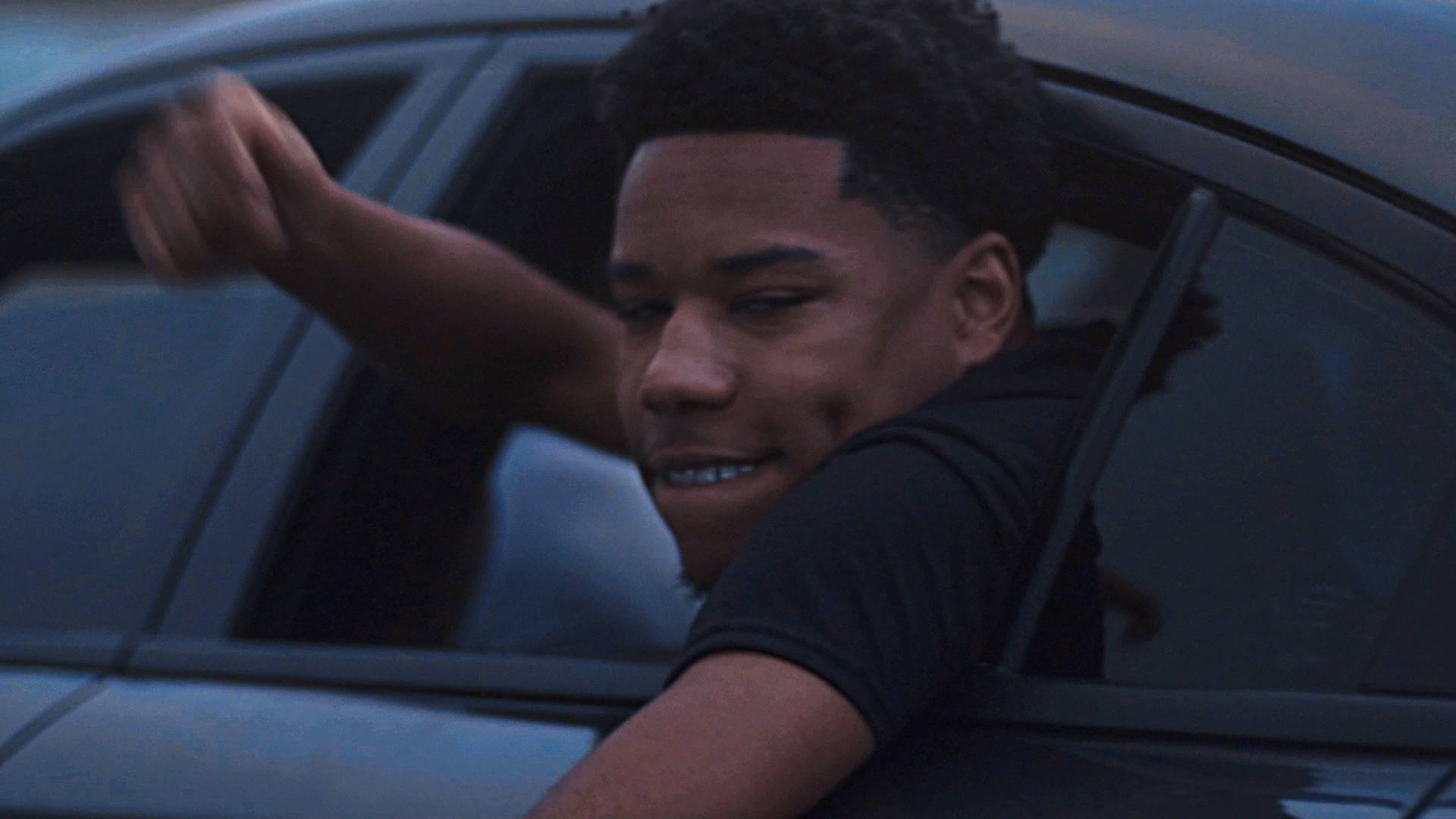 A Young Man Is Sitting In A Car And Waving His Hand Background