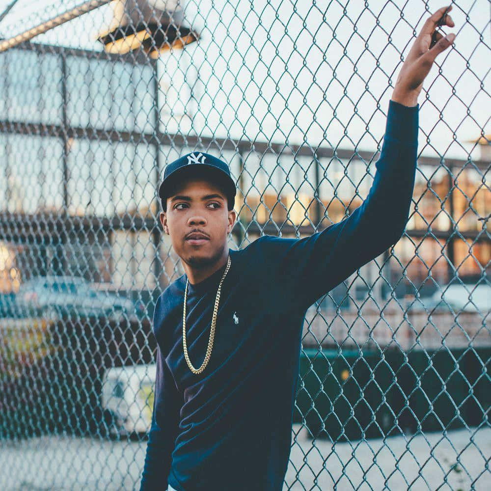 A Young Man Leaning Against A Chain Link Fence Background