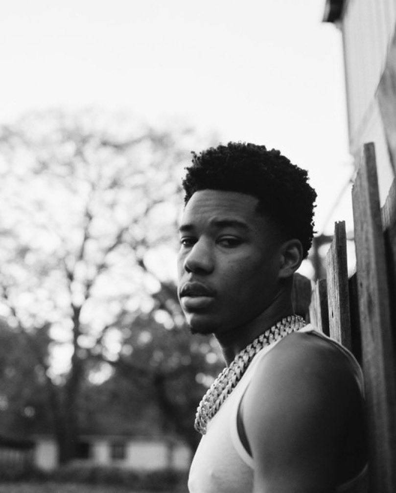 A Young Man Leaning Against A Fence Background