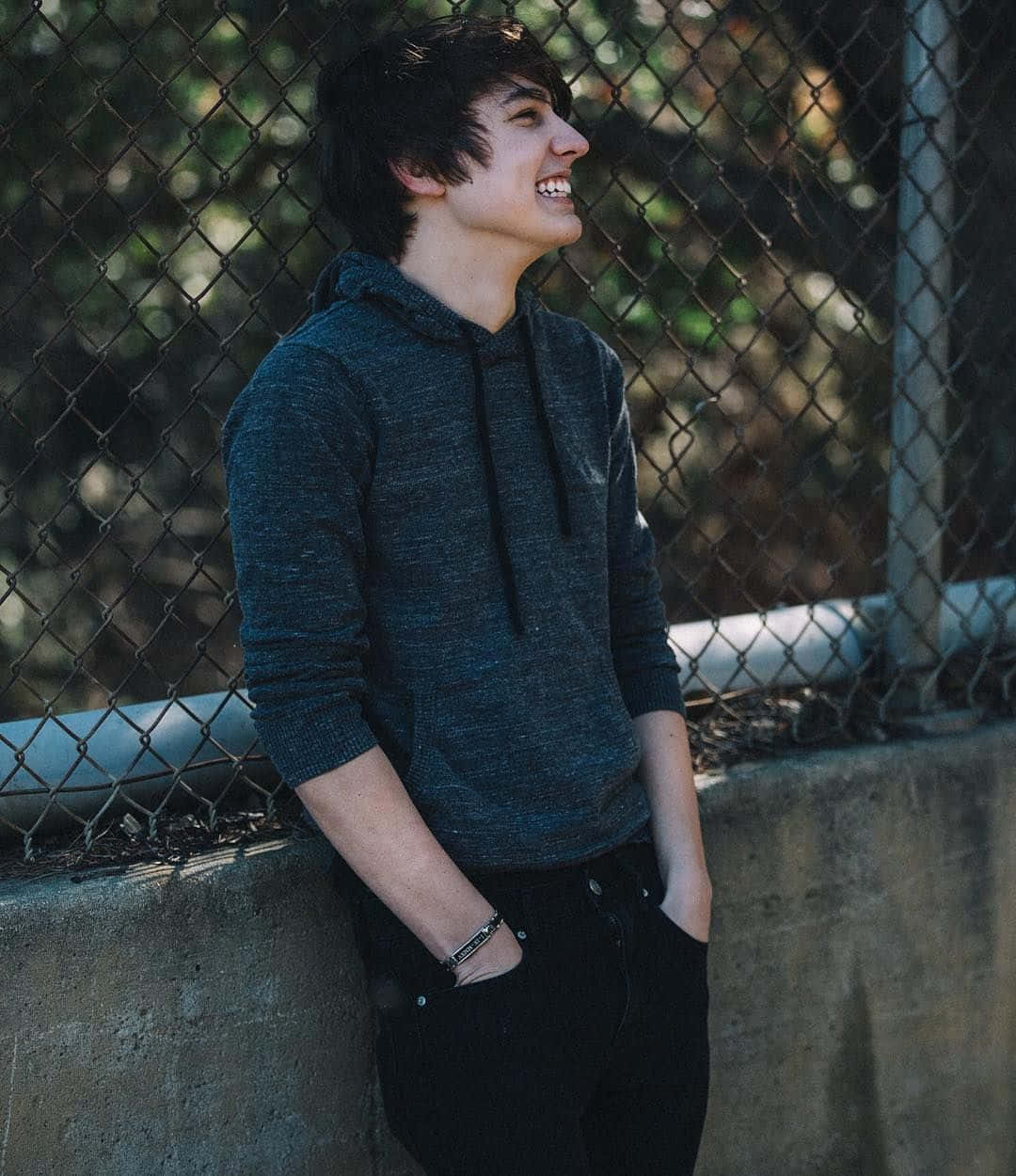 A Young Man Leaning Against A Fence Background