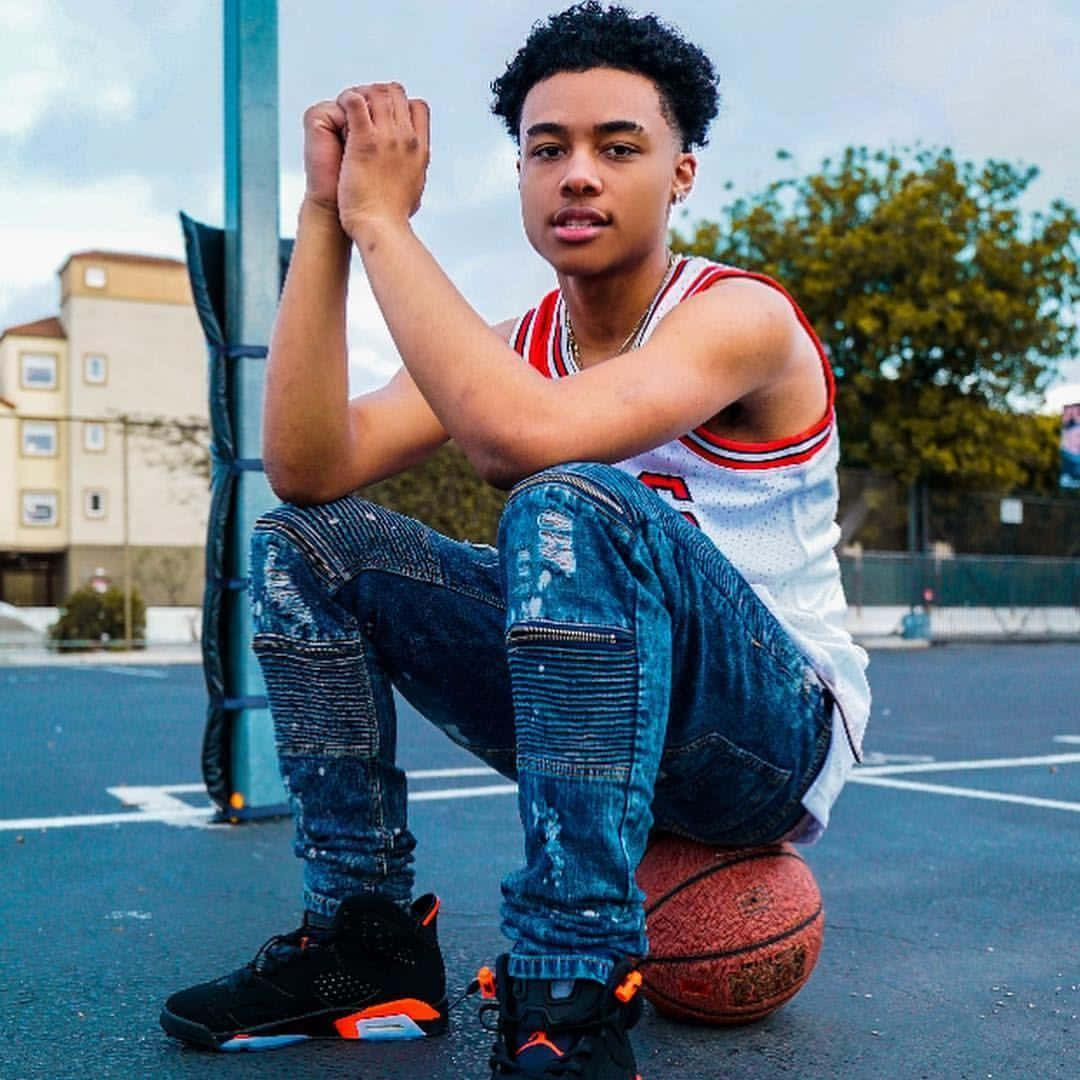 A Young Man Sitting On A Basketball Ball Background