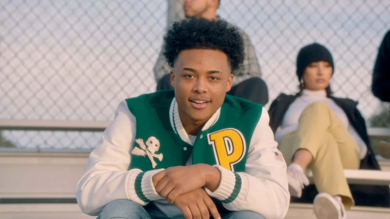 A Young Man Sitting On A Bench With Other People Background
