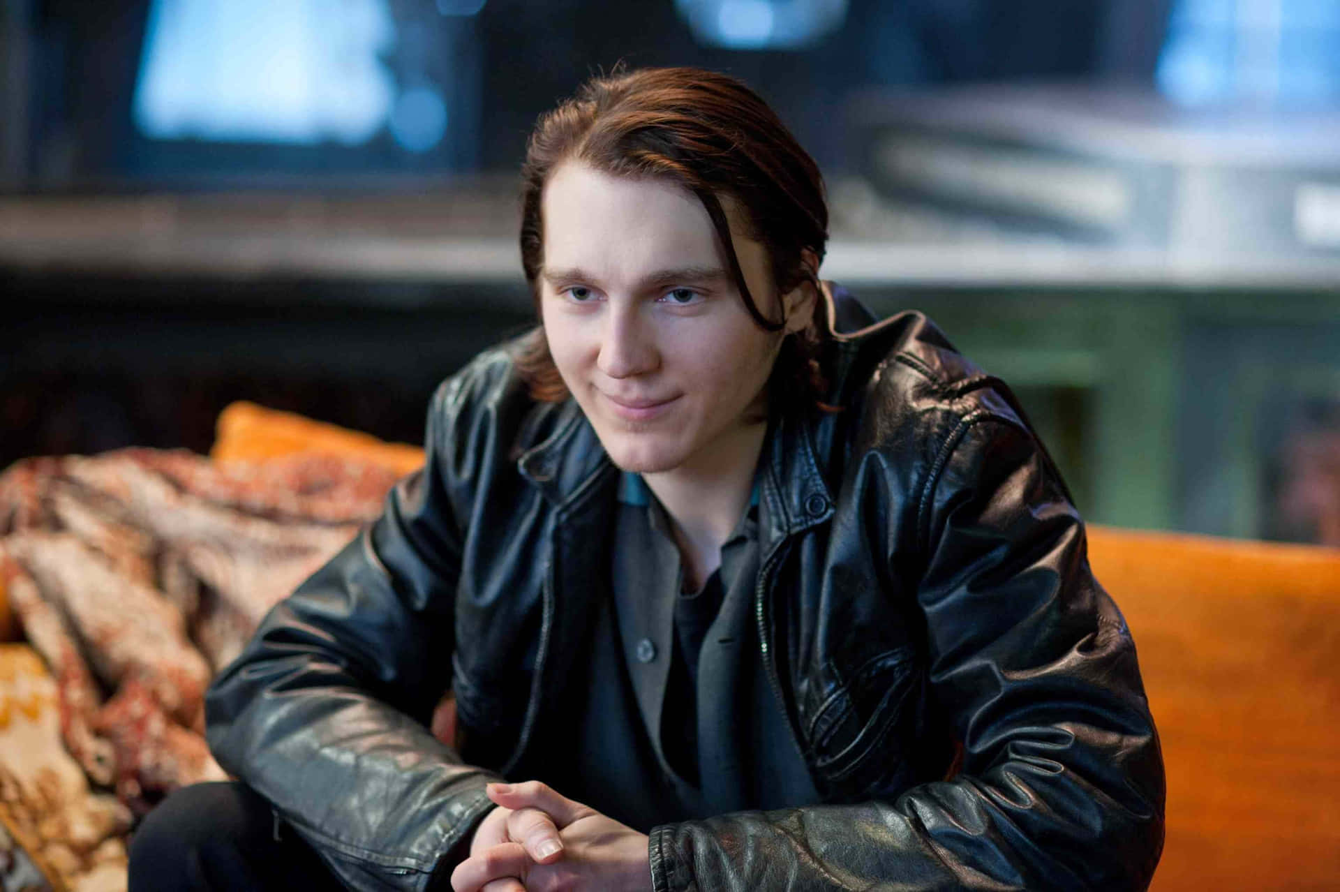 A Young Man Sitting On A Couch In A Leather Jacket Background