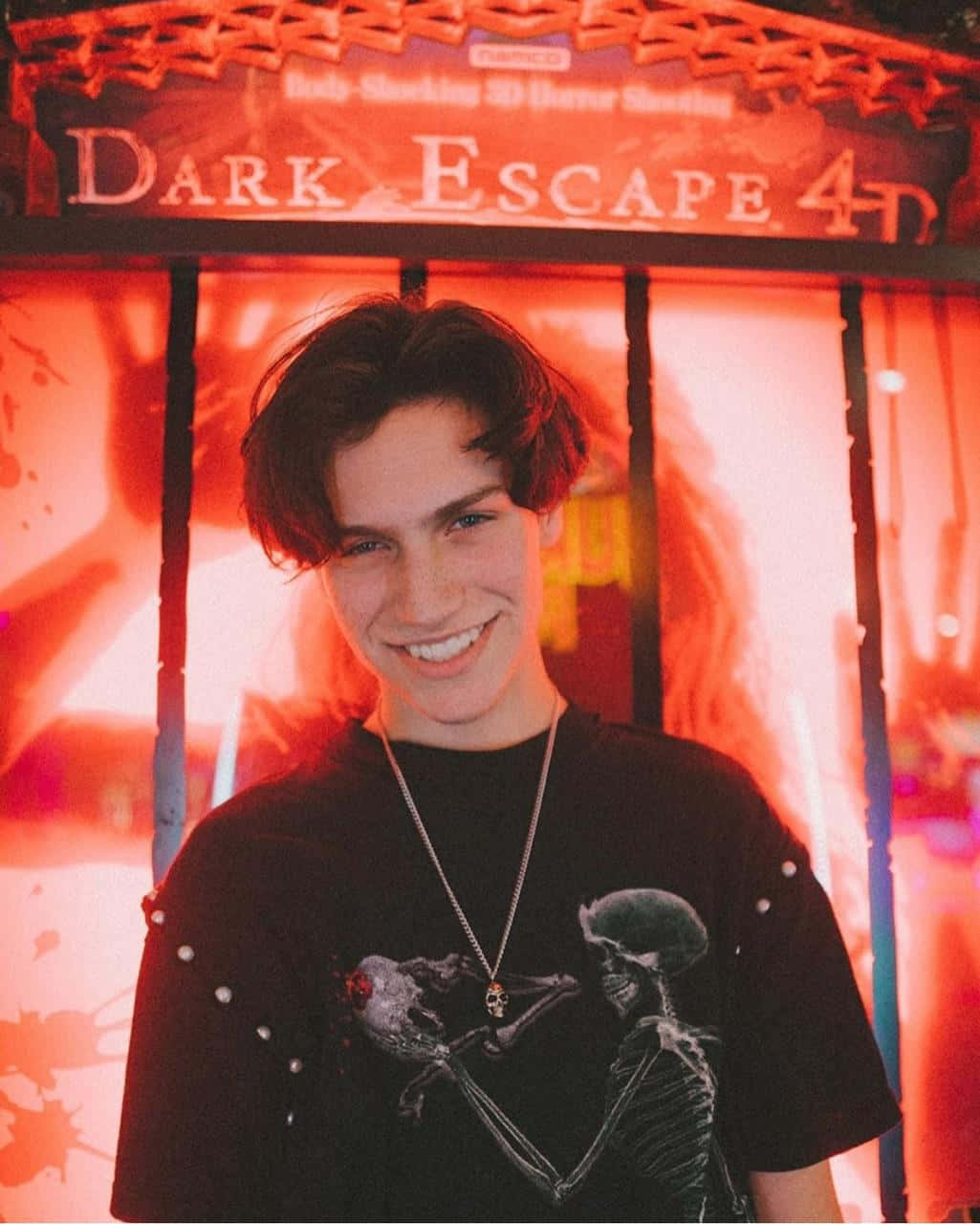 A Young Man Smiling In Front Of A Dark Escape Sign
