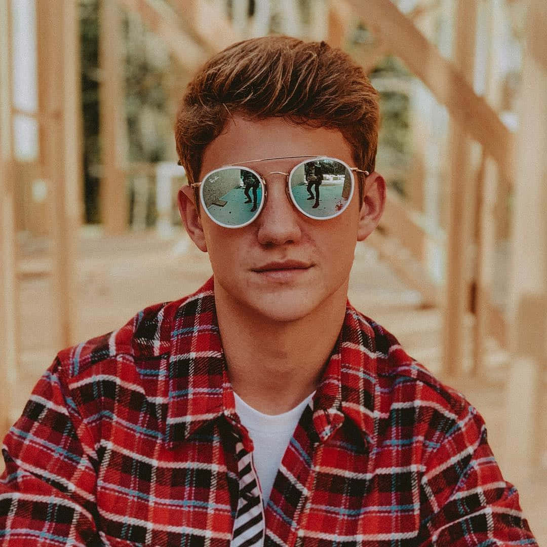 A Young Man Wearing Sunglasses And A Plaid Shirt Background