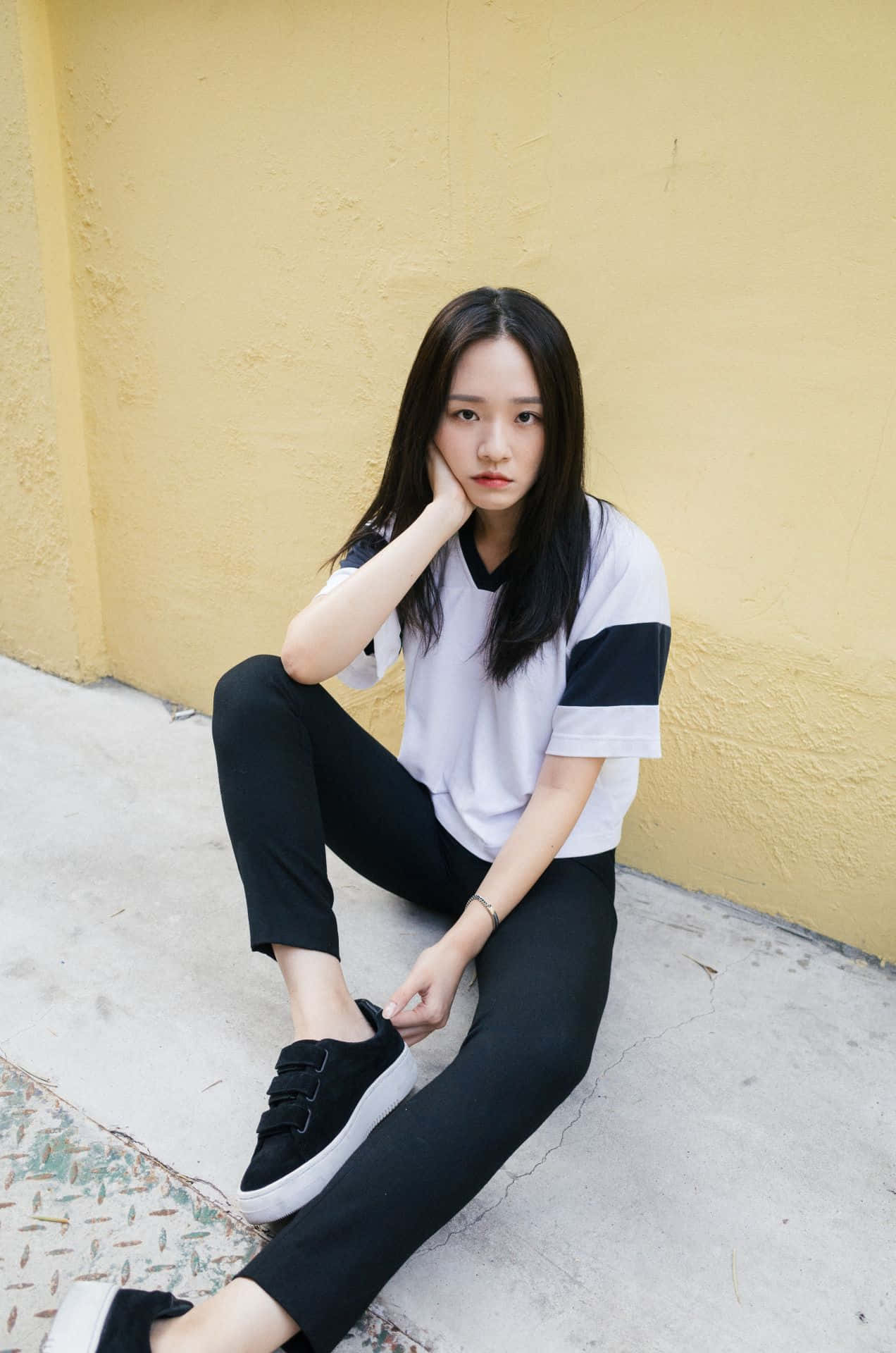 A Young Woman Sitting On The Ground Wearing Black Pants And White T - Shirt Background