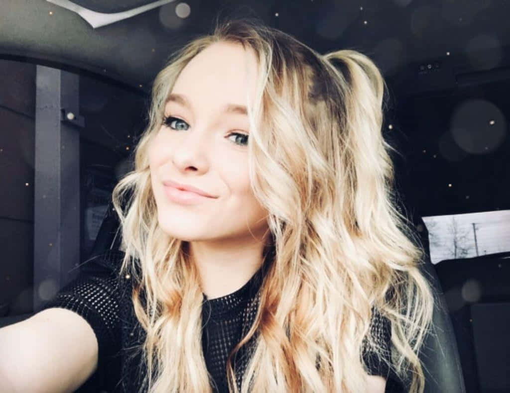 A Young Woman With Long Blonde Hair Sitting In A Car Background