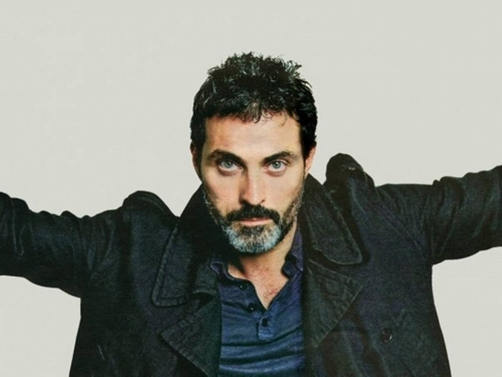 Actor Rufus Sewell Sporting A Black Denim Jacket Background