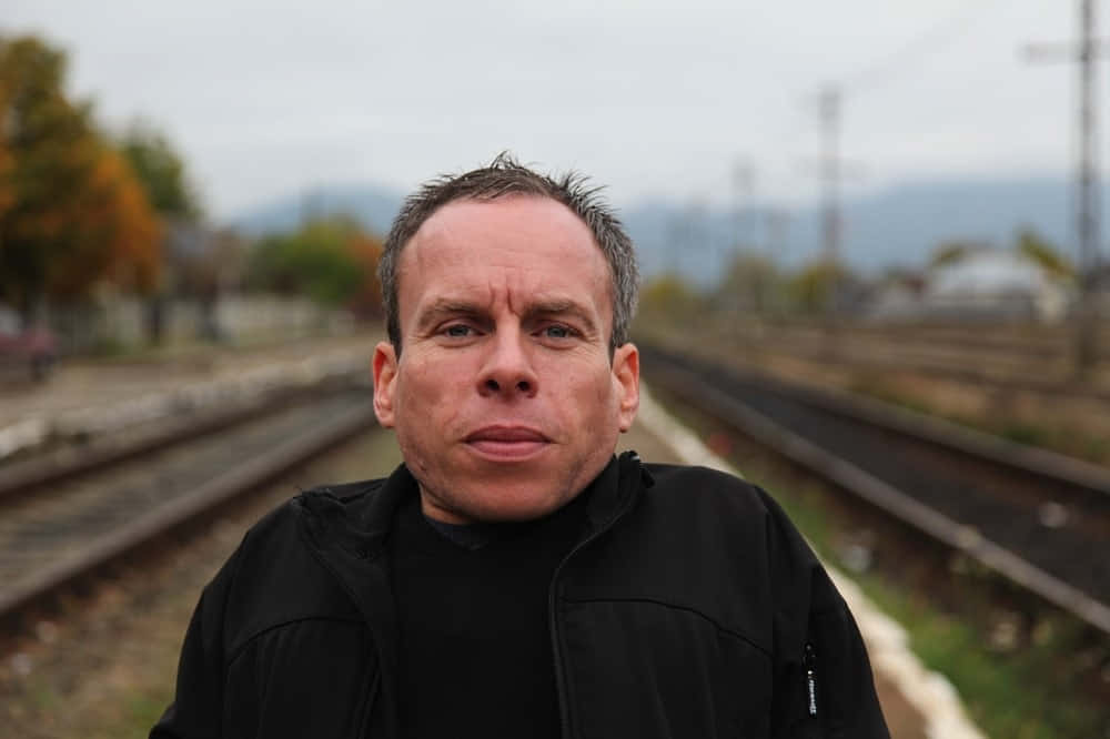 Actor Warwick Davis Posing At An Event Background