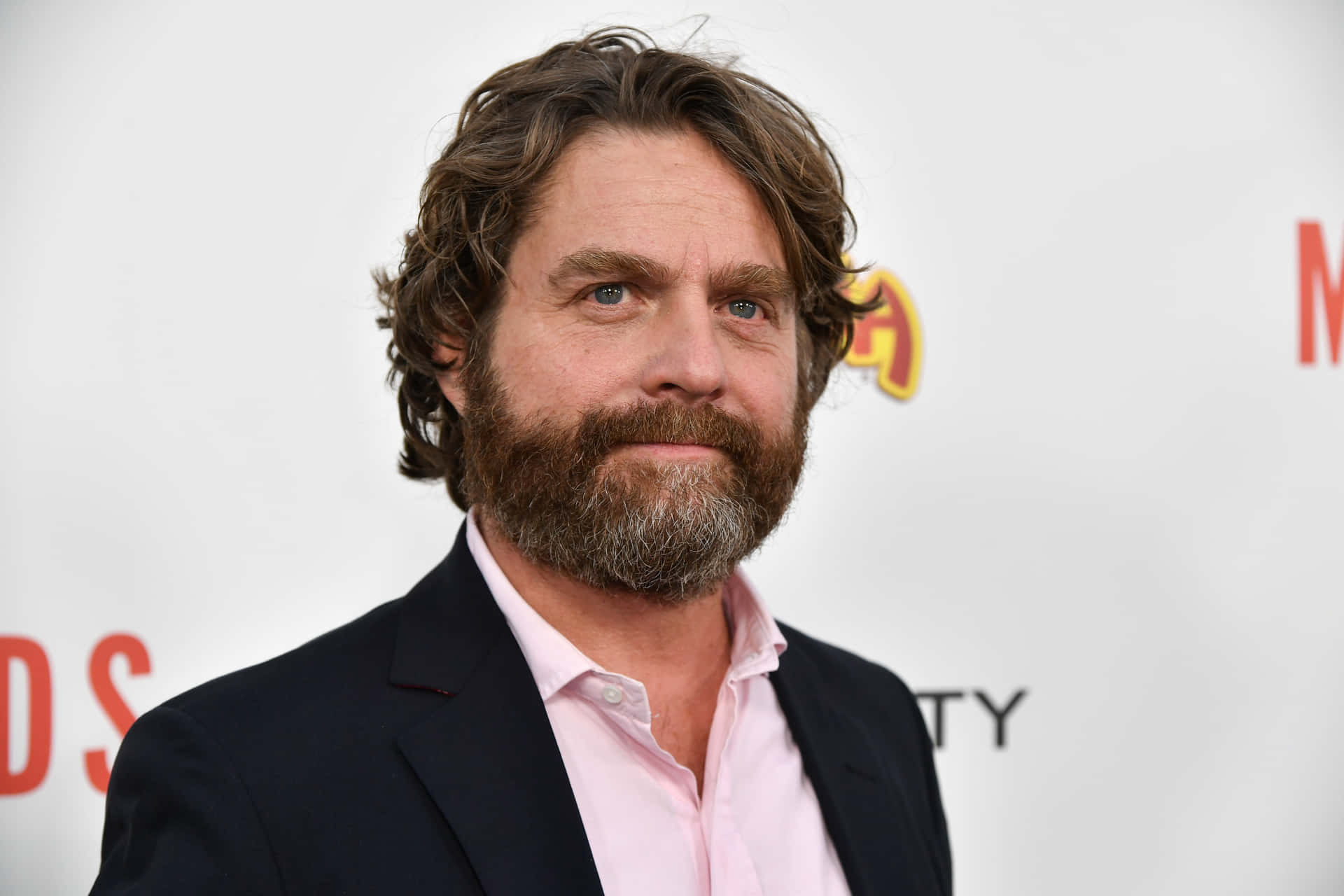 Actor Zach Galifianakis Smiling On The Red Carpet Background
