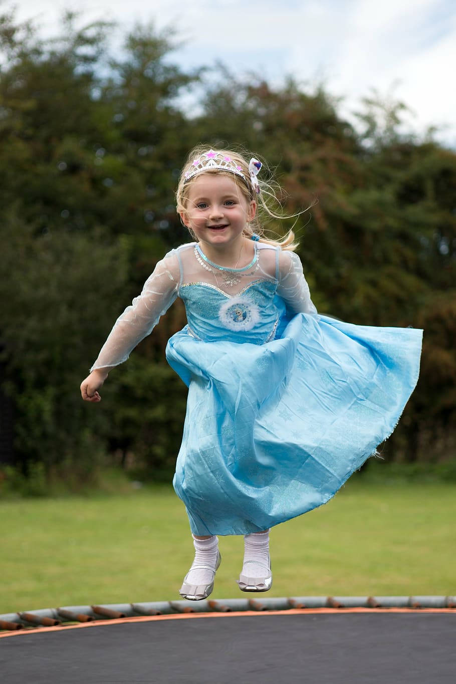 Adorable Girl In Gown Jumping On Trampoline Background