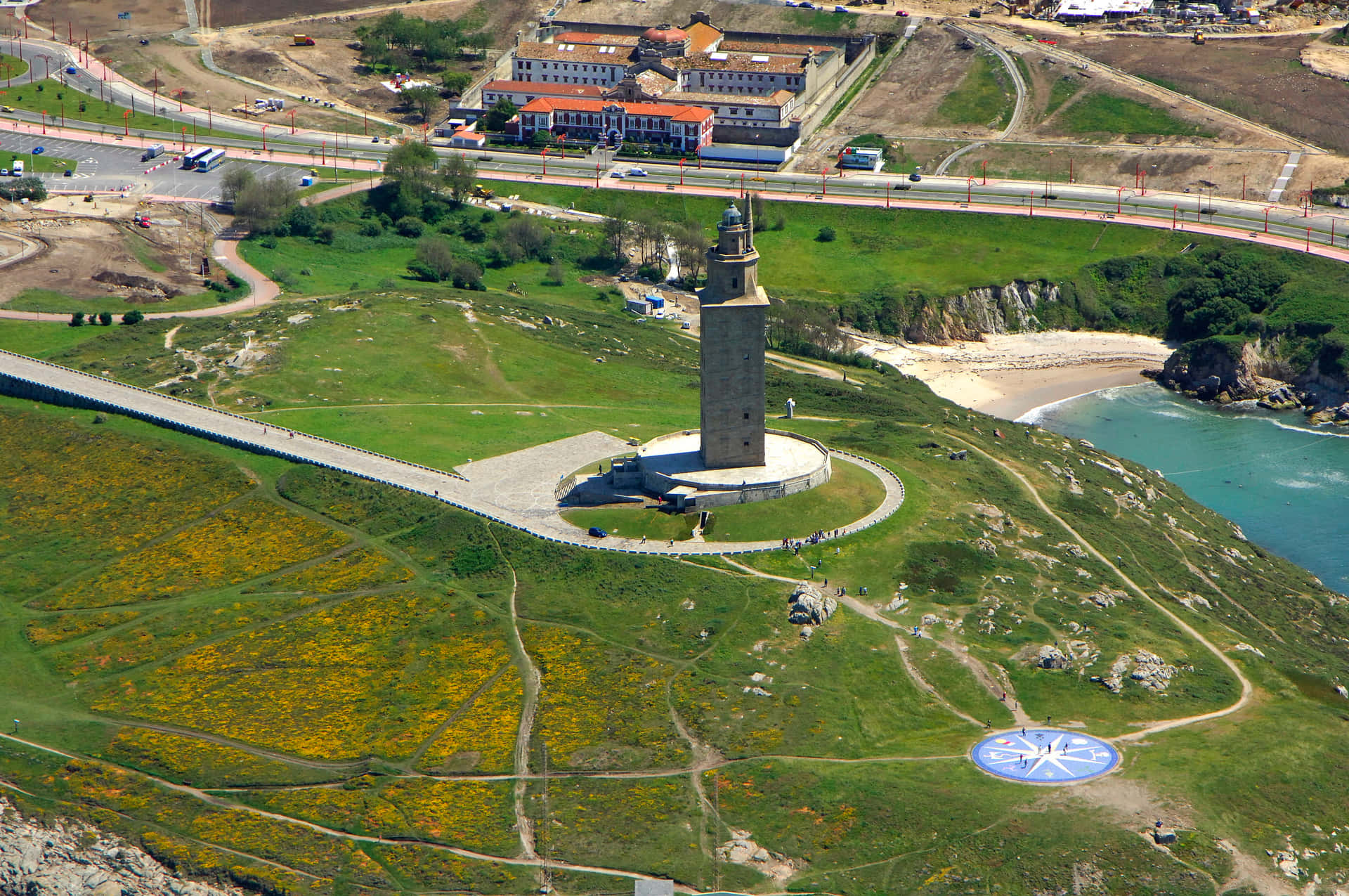 Aerial View Of The Majestic Tower Of Hercules Surrounded By Lush Green Grass Background