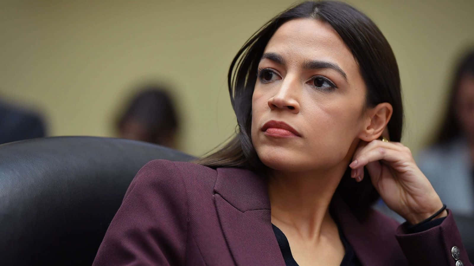 Alexandria Ocasio-cortez Elegantly Presenting In Maroon Suit Background