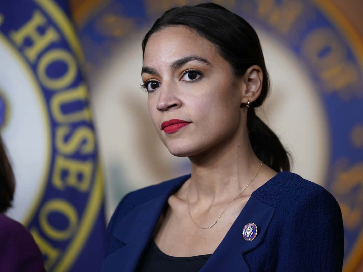 Alexandria Ocasio-cortez In Front Of Blue Backdrop Background