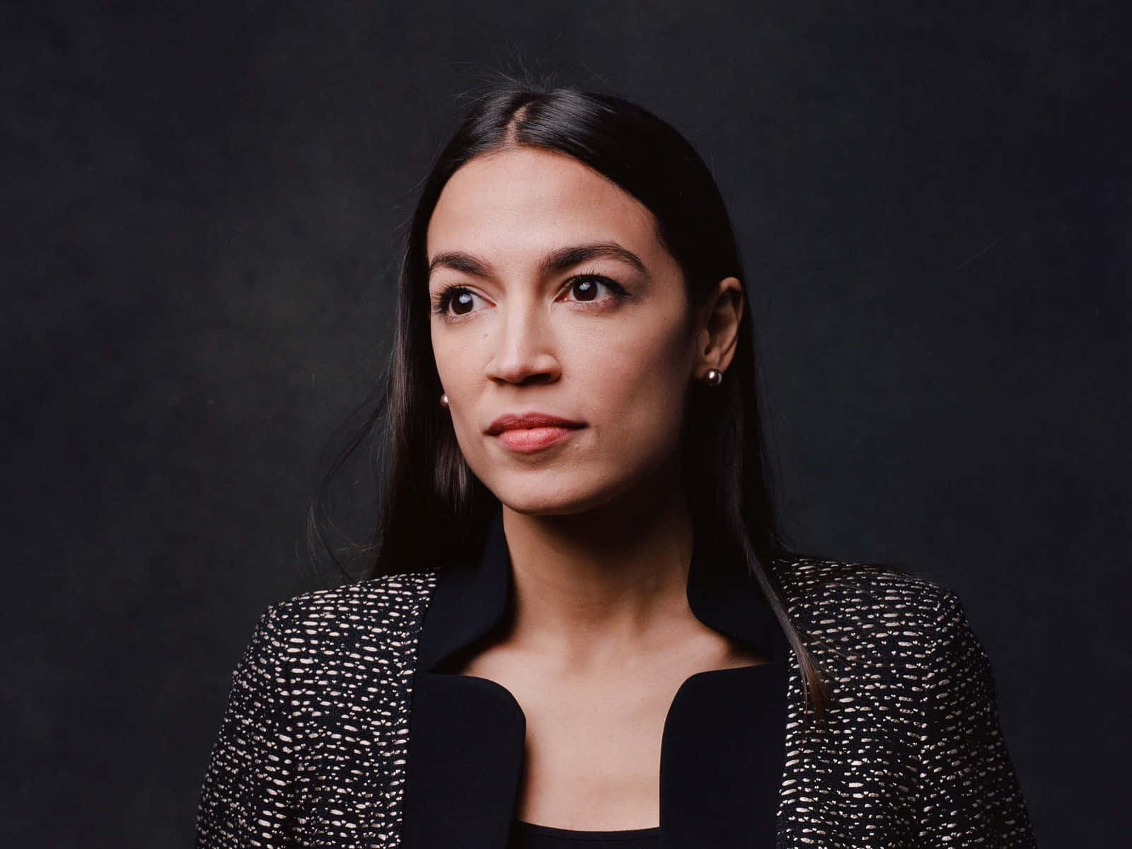 Alexandria Ocasio-cortez Posing Against A Black Backdrop Background