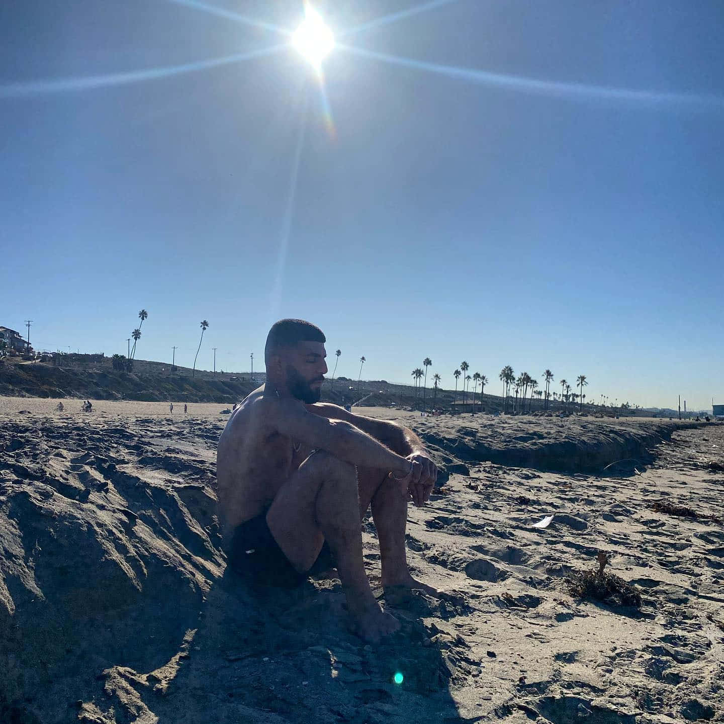 Amir Albazi Sitting On Sandy Beach Background
