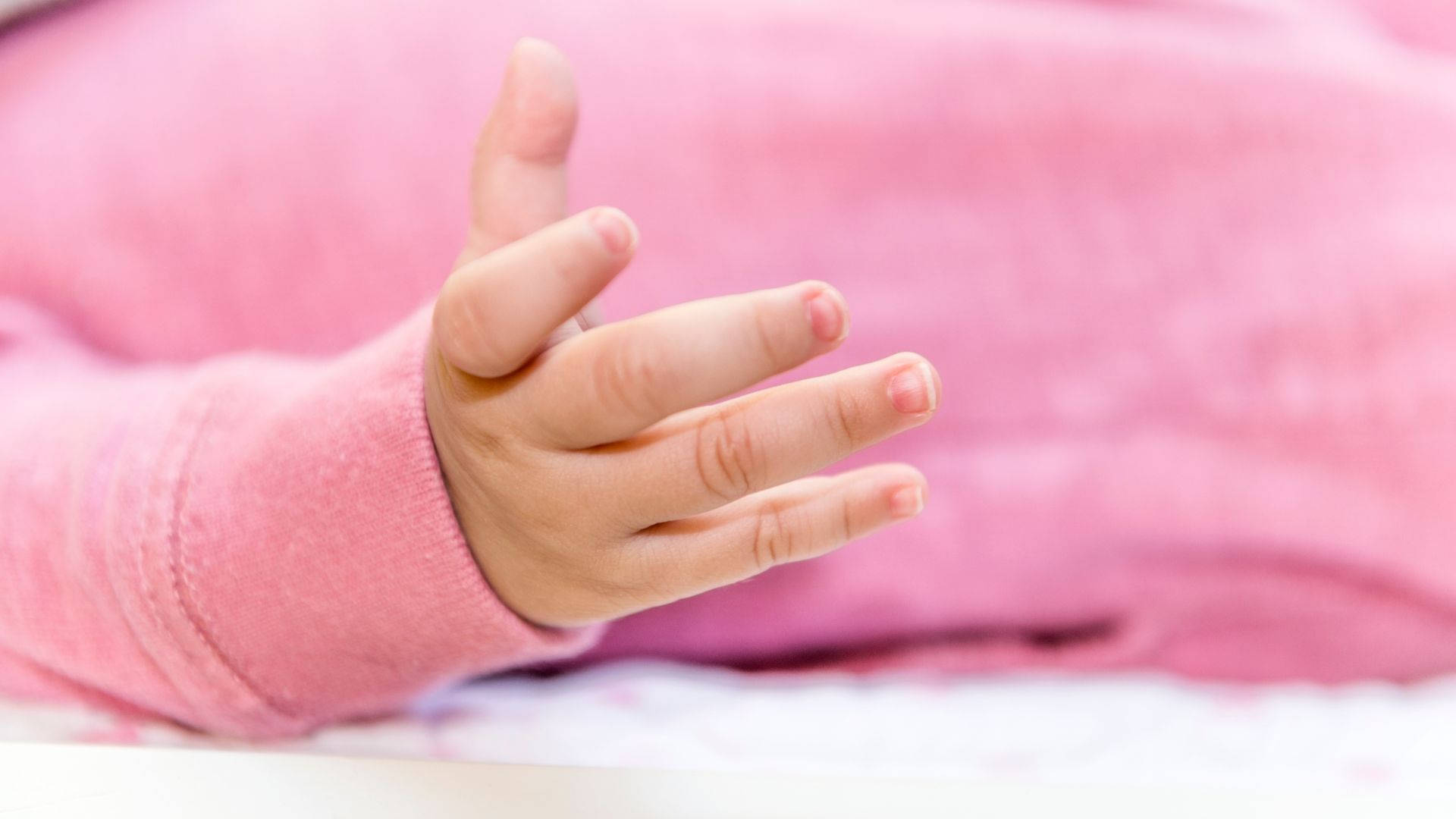 An Adorable Baby Hand In A Pink Onesie Background