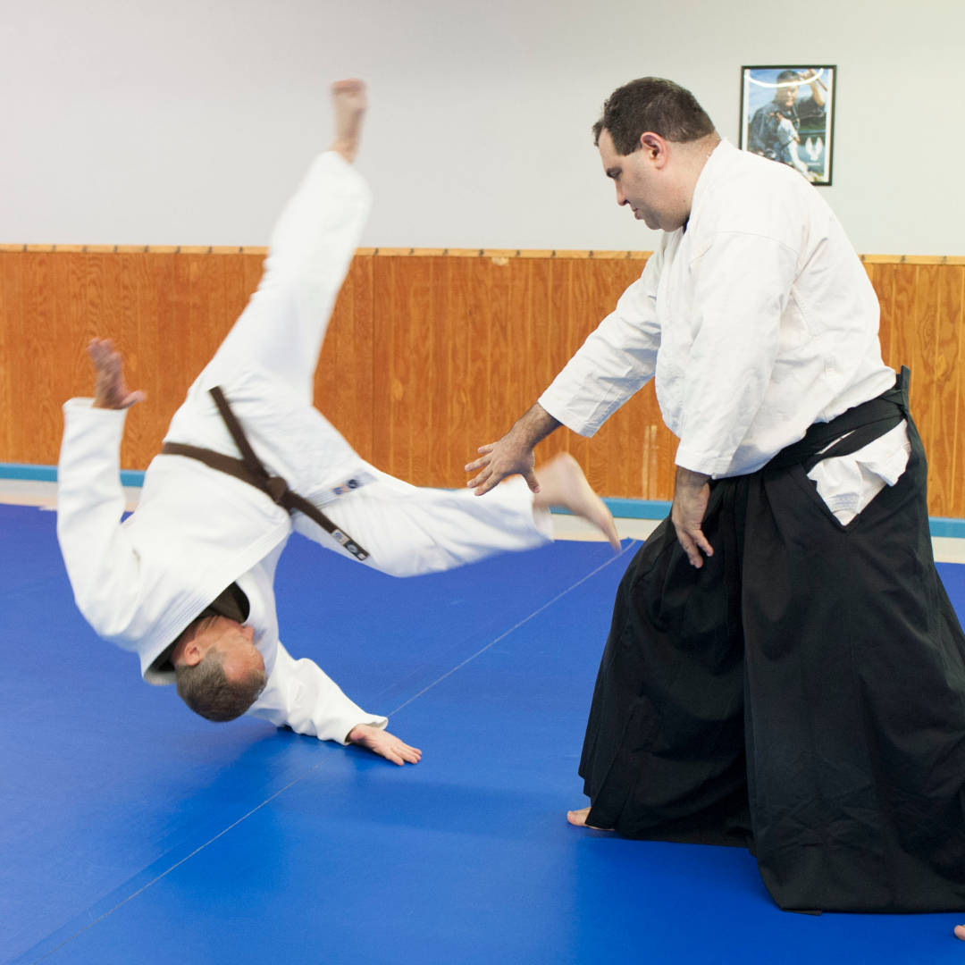 An Aikido Practitioner Executing A Dynamic Aiki-nage Technique In A Dojo Background