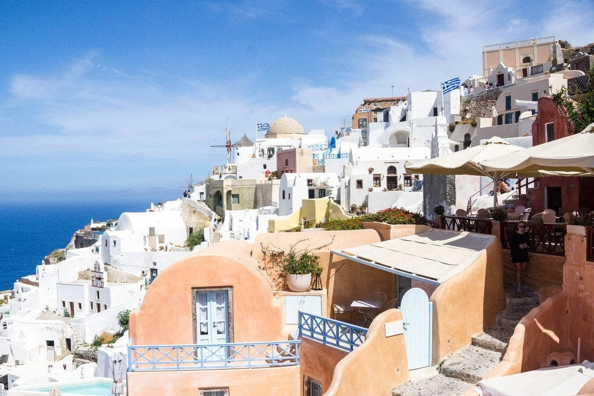 An Exquisite View Of Santorini's Iconic Blue-domed Churches And Whitewashed Houses Overlooking The Shimmering Aegean Sea. Background