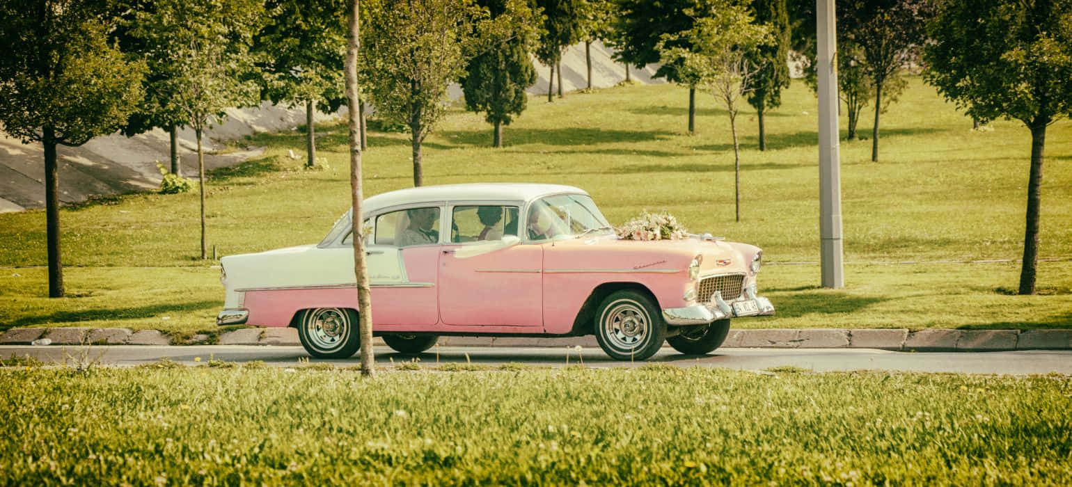 An Eye-catching Pink Vintage Car Parked On A Cobblestone Street Background