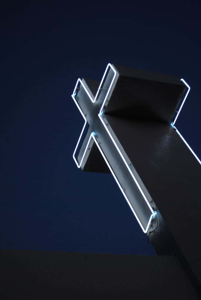 An Illuminated Neon Cross Surrounded By Darkness. Background