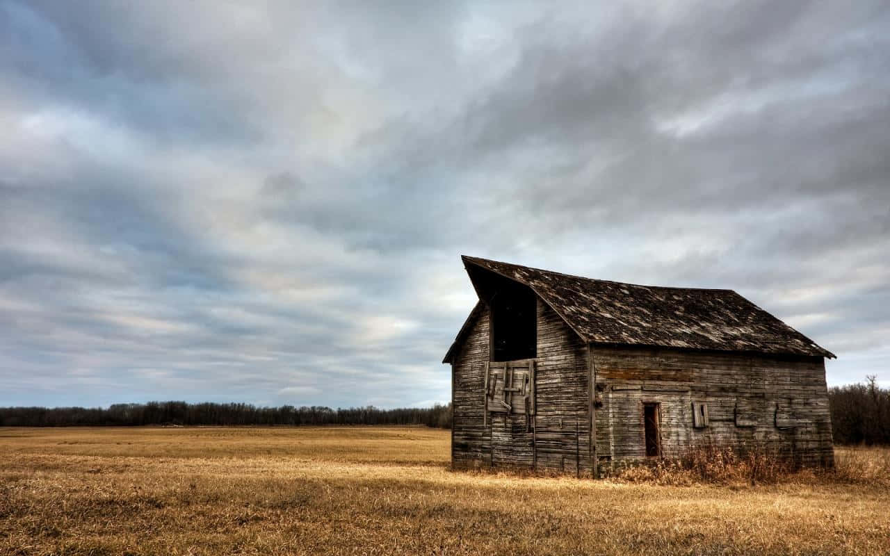 An Old Barn Sits In A Field Under A Cloudy Sky Background