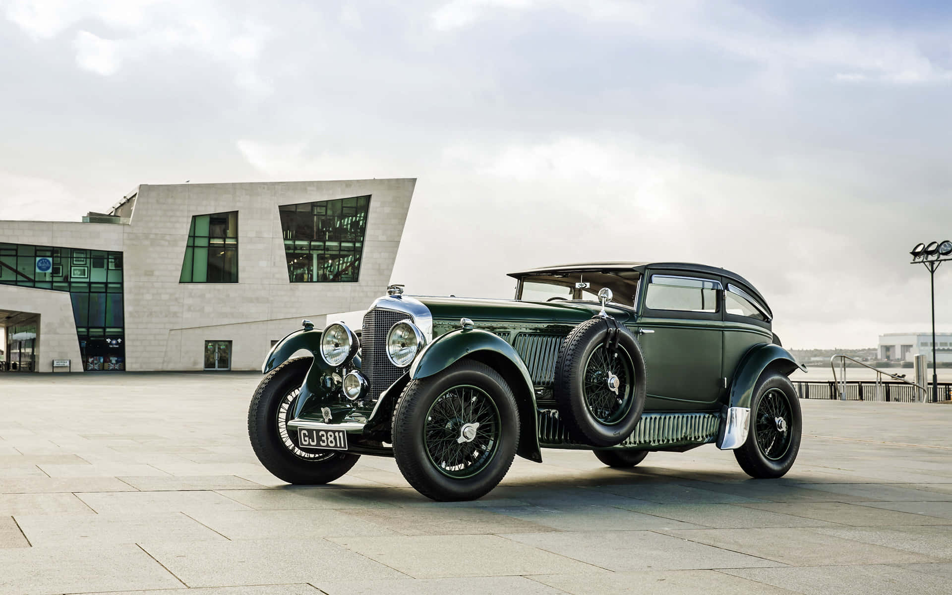 An Old Green Car Parked In Front Of A Building Background