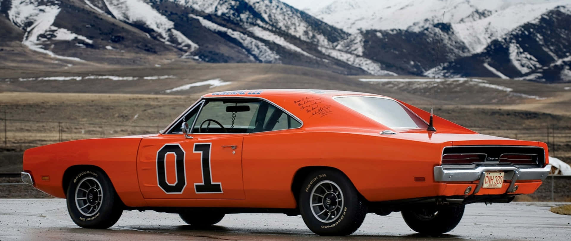 An Orange Dodge Charger Is Parked In Front Of Mountains Background