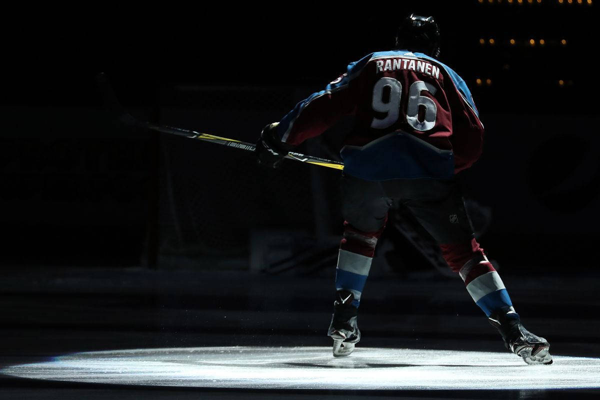 Back Shot Of Mikko Rantanen Raising Hockey Stick Under The Spotlight Background