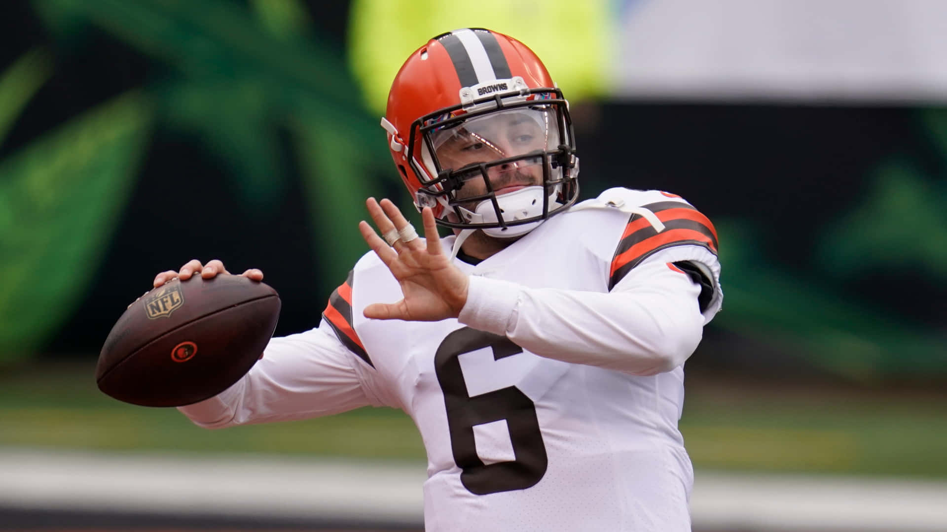 Baker Mayfield Throws Ball In The Field Background