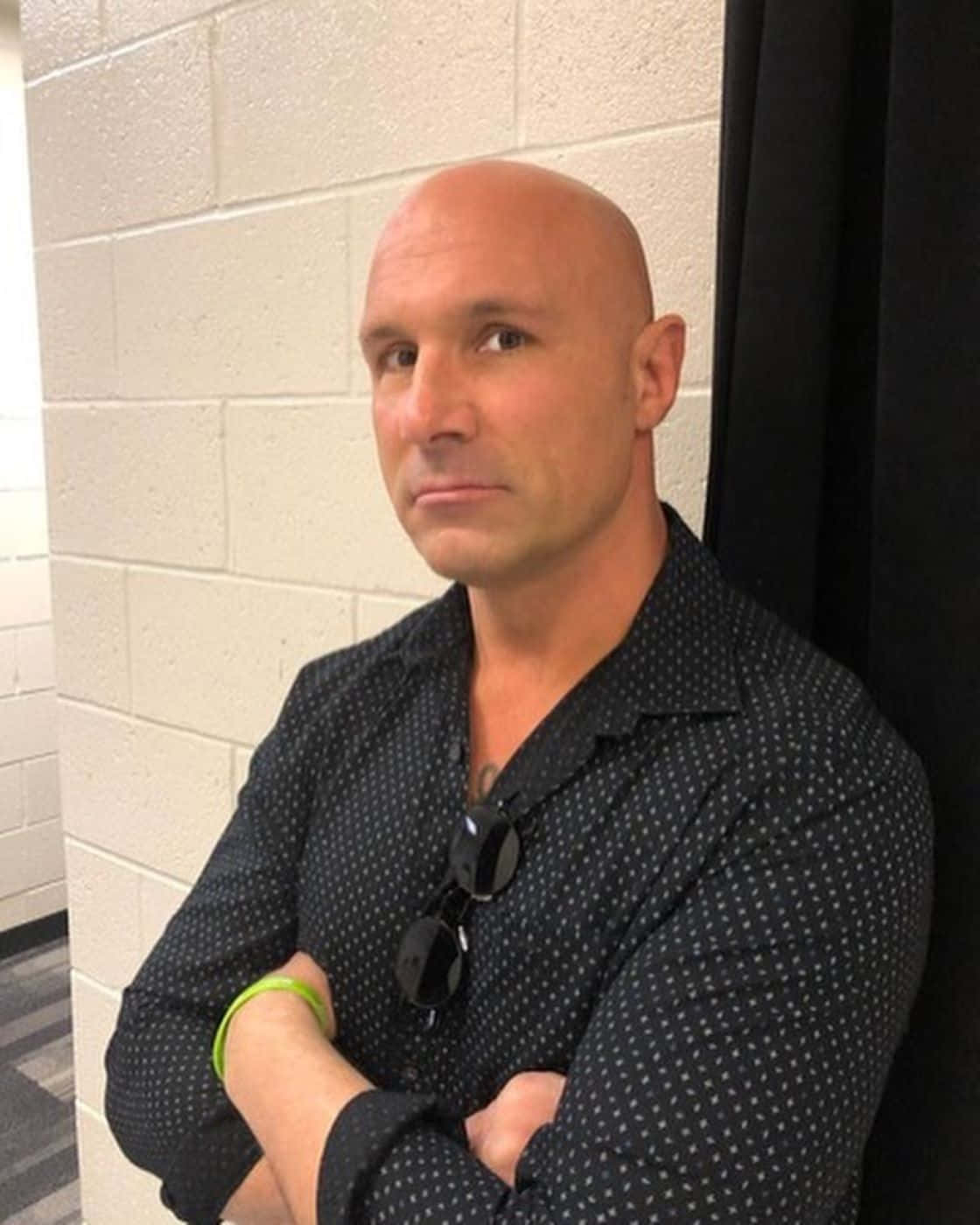 Bald Manin Black Shirt Leaning Against Wall Background