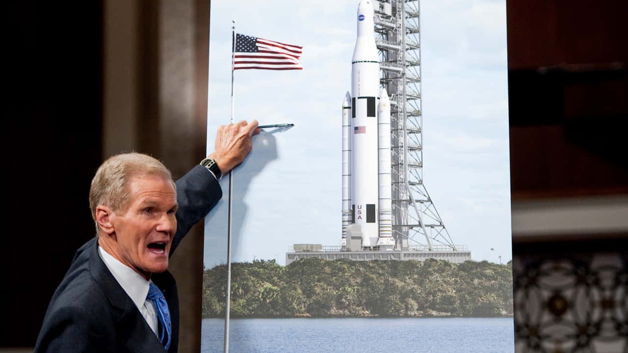 Bill Nelson Pointing At A Nasa Rocket Background