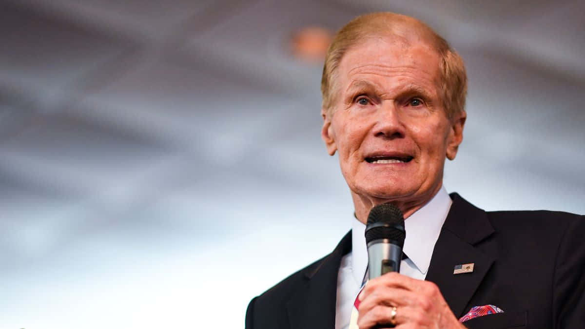 Bill Nelson With Microphone And Gray Backdrop Background