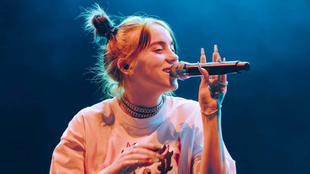 Billie Eilish Sits Surrounded By Her Laptop And Gear Background