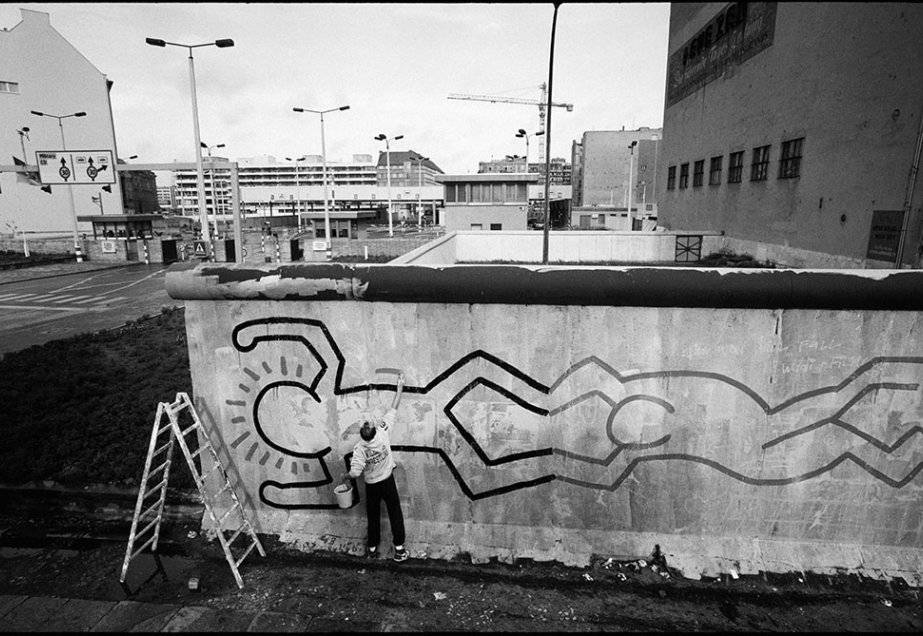 Black And White Graffiti Keith Haring Working On A Wall Background